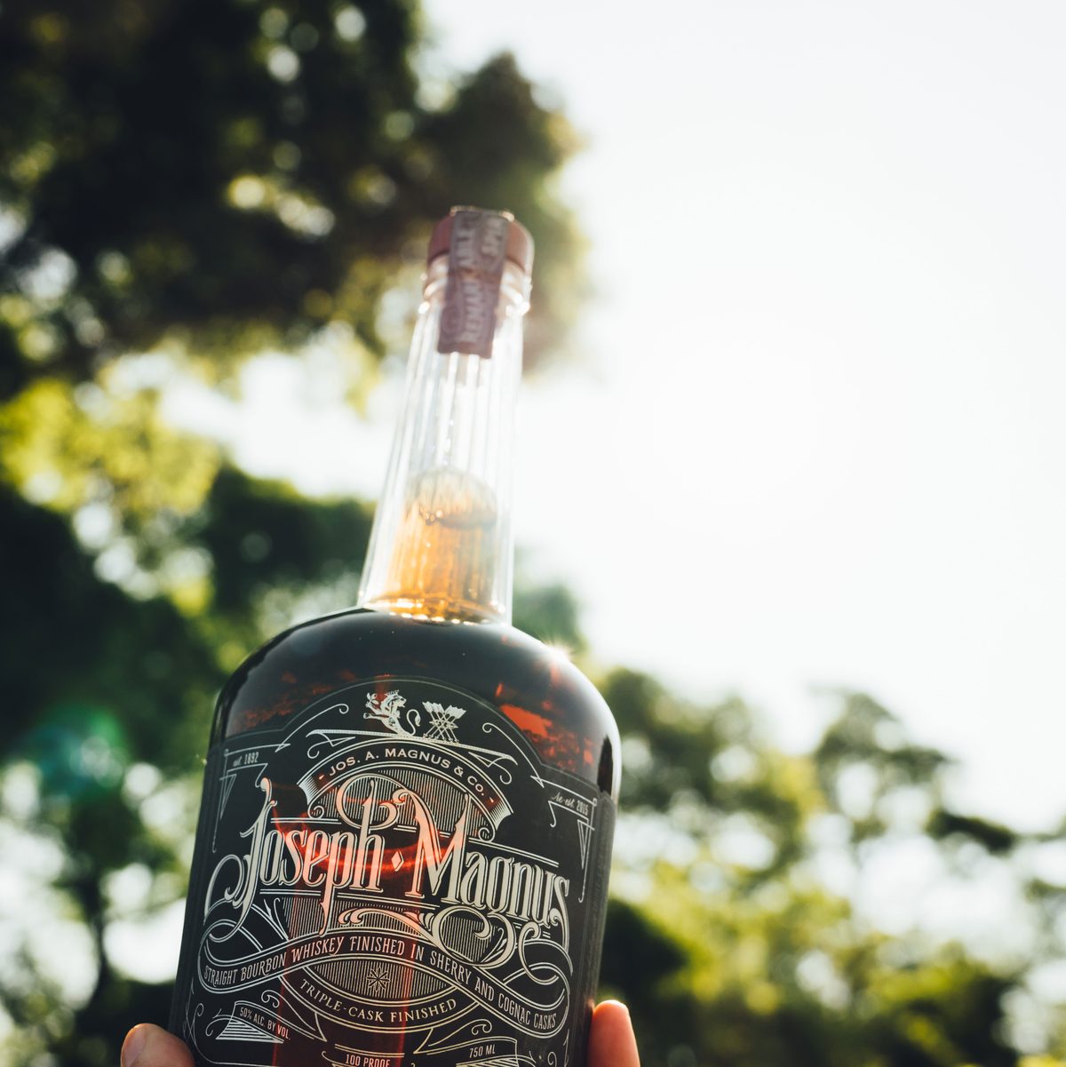 A bottle of Joseph Magnus Bourbon held up outdoors